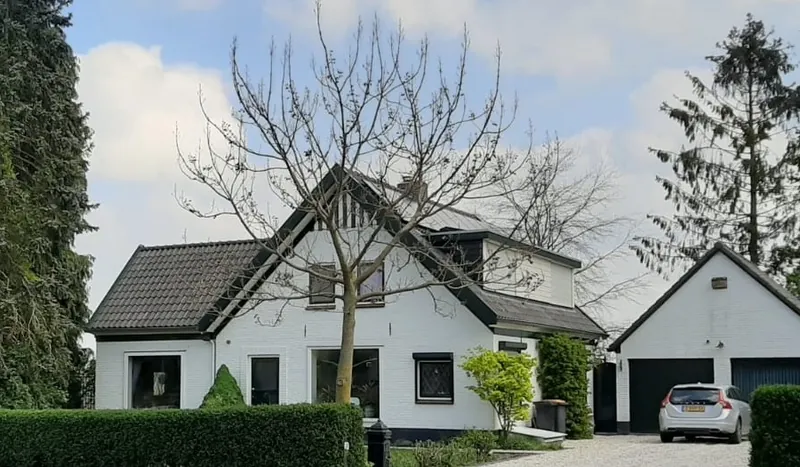 Een wit vrijstaand huis met een donkere kap en een garage