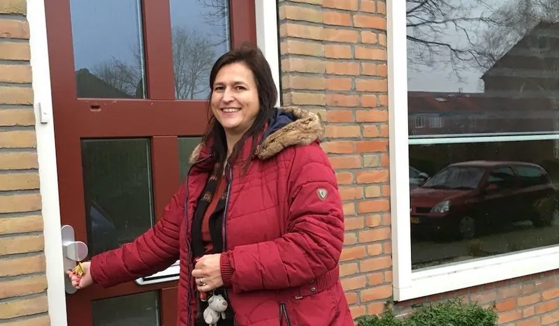 Een vrouw opent met een sleutel de rode voordeur van haar huis