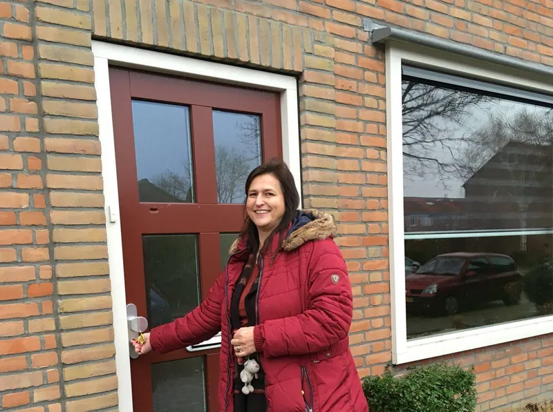 Een vrouw opent met een sleutel de rode voordeur van haar huis
